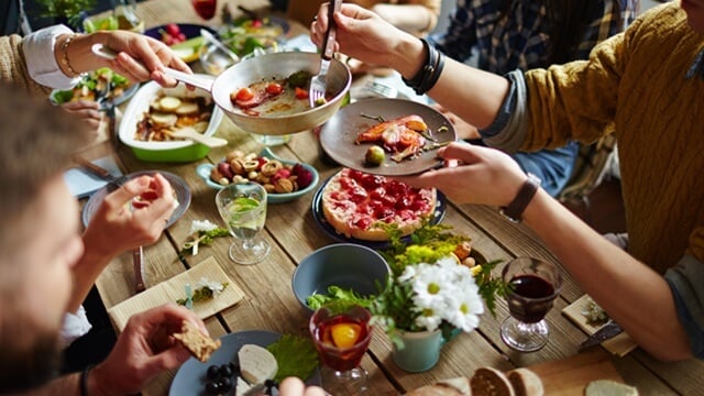 Group of friends sharing a meal at a rustic wooden table with assorted dishes and drinks