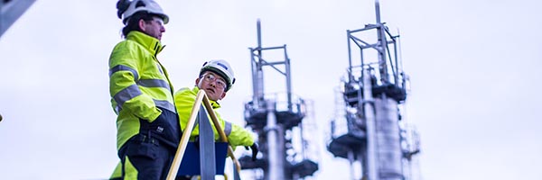 Two engineers discussing outdoors at industrial plant with grey sky in the background